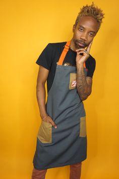 a man in an apron poses for the camera with his hand on his chin and looking at the camera