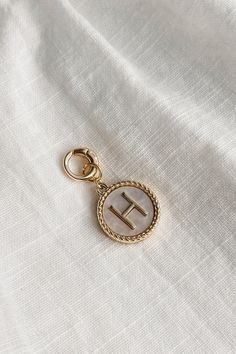 Image shows the 'H' alphabet charm against a white background. Charm is a gold circle with pearlescent center and has gold letter H in the center. Gold Round Jewelry With Logo Charm, Everyday Gold Pearl Charm, Gold Initial Pendant Charms, Gold Round Pendant Charm With Pearl, Gold Monogram Charms For Gifts, Trendy Gold Monogram Jewelry, Trendy Gold Jewelry With Monogram, Elegant Gold Initials Charms, Elegant Gold Charms With Initials