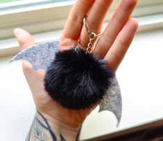 a hand holding a black pom - pom keychain in front of a window