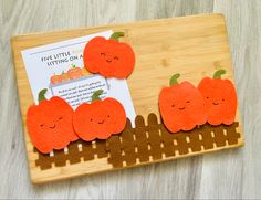 three felt pumpkins sitting on top of a cutting board next to a piece of paper