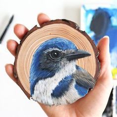 a hand holding a piece of wood with a blue and white bird painted on it