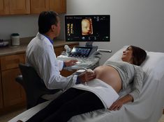 a pregnant woman laying in a hospital bed next to a doctor who is looking at her monitor