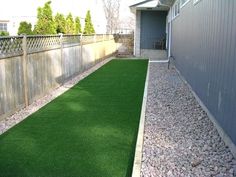 an artificial lawn in the back yard with gravel and grass around it, next to a fence