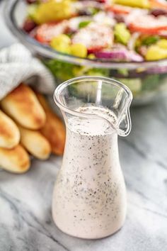 a glass pitcher filled with dressing next to a salad