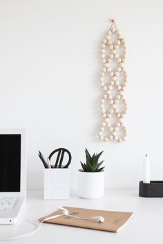 a laptop computer sitting on top of a white desk next to a wooden bead wall hanging