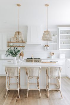 Modern minimalist kitchen with white cabinets, wicker pendant lighting, and an island with bar stools. Bright, airy, and elegant minimalist kitchen design. Simple Coastal Kitchen, White Airy Kitchen, White Warm Kitchen, Modern Coastal Farmhouse Kitchen, Neutral Modern Kitchen, Serene Kitchen, White Coastal Kitchen, Minimalist Kitchen Ideas, Minimal Ideas