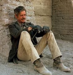 a man sitting on the ground next to a stone wall