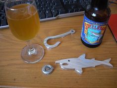 a bottle opener next to a glass filled with beer and a shark keychain