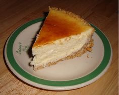 a piece of cheesecake on a green and white plate sitting on a wooden table