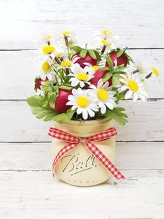 a mason jar filled with daisies and apples on top of a white wooden table