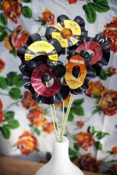 a vase filled with assorted vinyl records on top of a table next to a wall