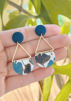 a pair of blue and white earrings with leaves on the front, hanging from a gold - plated earwire