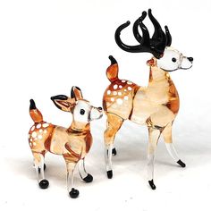 two glass deer figurines standing next to each other on a white surface,