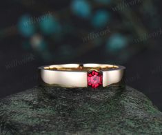 a close up of a ring with a red stone in the center on a rock