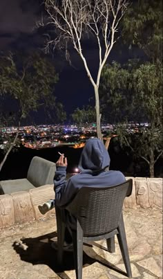 a person sitting in a chair on top of a hill at night with the city lights behind them