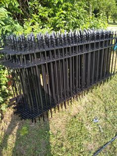 a fence made out of black iron rods in the middle of some grass and trees