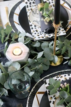 the table is set with black and white plates, silverware, greenery and candles