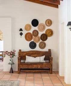 a wooden bench sitting in front of a wall with hats on it's back