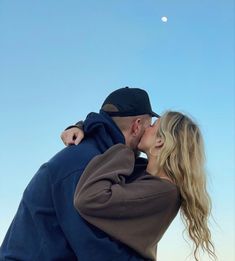 a man and woman kissing each other in front of a blue sky with the moon behind them