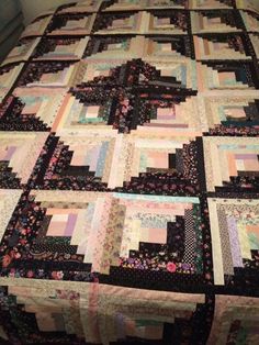 a quilt is laying on top of a bed with black and pink colors in it