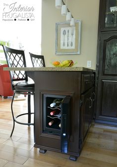 a wine cooler in the middle of a kitchen island with chairs around it and a painting on the wall