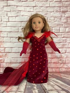 a doll with long hair wearing a red dress and red gloves, standing in front of a brick wall