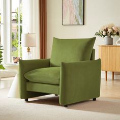 a green chair sitting in front of a window next to a vase with flowers on it