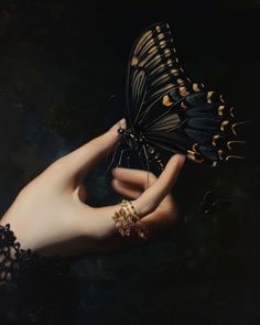 a woman's hand holding a butterfly in the dark, with gold accents on her arm