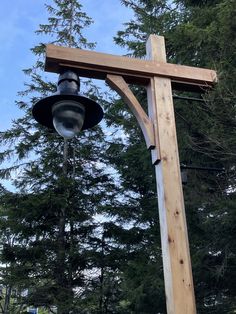 a wooden cross with a light hanging from it's side in front of some trees