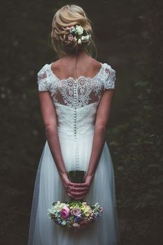 a woman in a white wedding dress holding a bouquet and wearing a flower crown with her hands behind her back