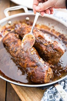 someone is spooning some meat with sauce in a pan on a wooden table,