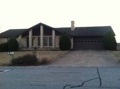 a large house sitting on the side of a road in front of a tree filled field