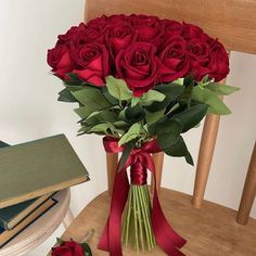 a bouquet of red roses sitting on top of a table next to a stack of books