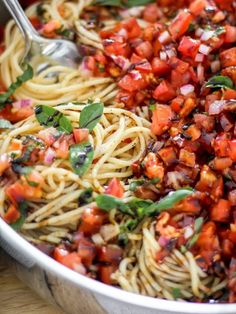 a bowl filled with pasta and vegetables on top of a wooden table next to a fork