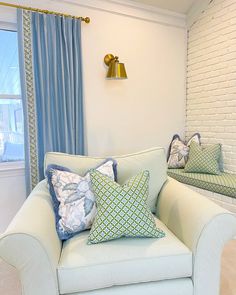 a white couch sitting next to a window with blue curtains and pillows on top of it