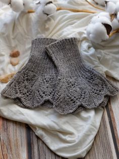 a pair of gray knitted socks sitting on top of a white blanket next to cotton balls