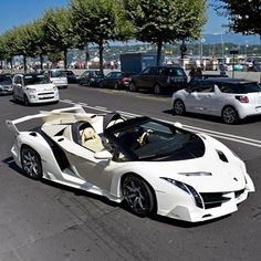 a white sports car is driving down the street with other cars in the back ground