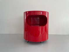 a red trash can sitting on top of a white table next to a wall and floor