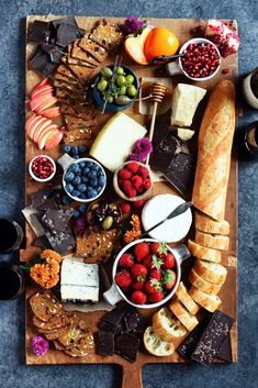 a wooden cutting board topped with lots of different types of breads and cheeses