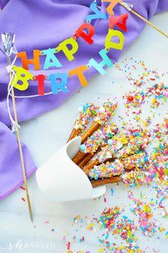 a birthday cake with sprinkles and candles on a white surface next to a purple napkin