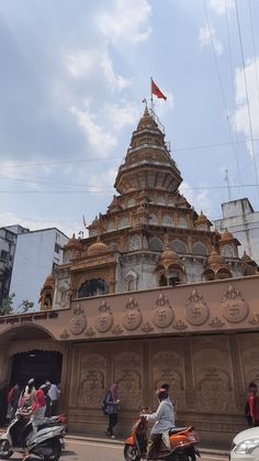 people are riding scooters in front of an ornately carved building with a flag on top