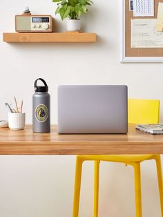 a laptop computer sitting on top of a wooden desk next to a yellow chair and potted plant