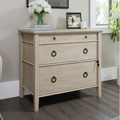 a wooden dresser with two drawers next to a chair and pictures hanging on the wall