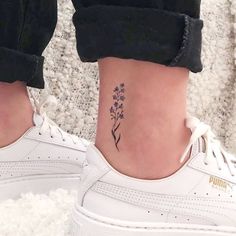 a woman's foot with a flower tattoo on her left ankle and white sneakers