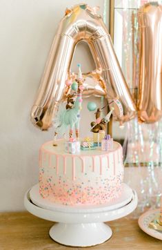 a birthday cake on a table with balloons and confetti