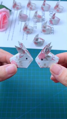 two hands are holding small origami pieces in front of a paper board with pink roses on it