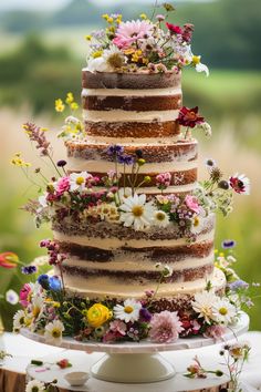 a multi layer cake with flowers on top is sitting on a white table in front of a green field