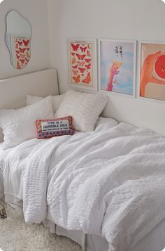 a bed with white sheets and pillows in a bedroom next to pictures on the wall