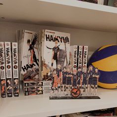 there are many anime books on the shelf next to a ball and some dvd's