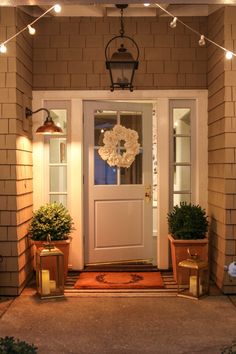 a front door with two potted plants and a wreath hanging on it's side